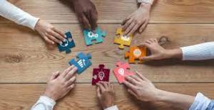 hands in a circle on a table, each touching a jigsaw piece